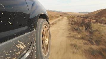 Close up side view of wheel spin on sandy gravel road with deserted landscape background video