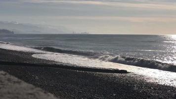 vista pacífica de la costa rocosa del mar negro con olas rompientes y silueta de la ciudad de batumi sobre el horizonte.