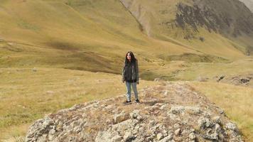 Attractive caucasian female backpacker stands on rock in scenic location and enjoys dramatic mountains video