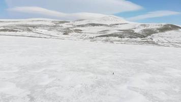 Luftaufnahme Solo-Person zu Fuß auf eisigem See allein mit verschneitem Landschaftshintergrund aus der Luftperspektive video