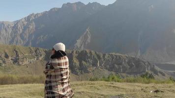Female caucasian person stands with blanket and enjoys mountain in solitude video