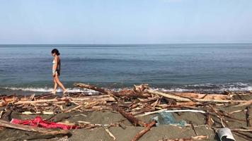 vista statica della spiaggia con donna caucasica che cammina in acqua e spiaggia del Mar Nero piena di rifiuti dopo la tempesta video