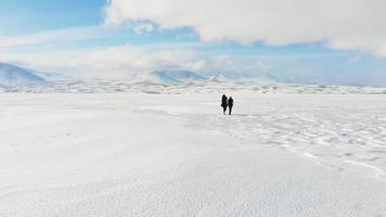 vuelo aéreo sobre la familia de turistas caminando sobre un lago blanco nevado congelado con un hermoso fondo panorámico video