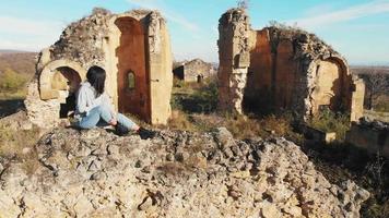 Female woman sits on historical site ruins and looks to remains of Sioni church. Samshvilde castle complex video