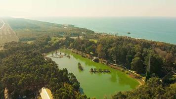 veduta aerea del parco dendrologico con lago d'acqua verde con sfondo blu del mare. ambiente e turismo georgia video