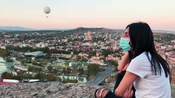 Close up panning view of young georgian woman wearing mask alone and watching Tbilisi city panorama during pandemic. video