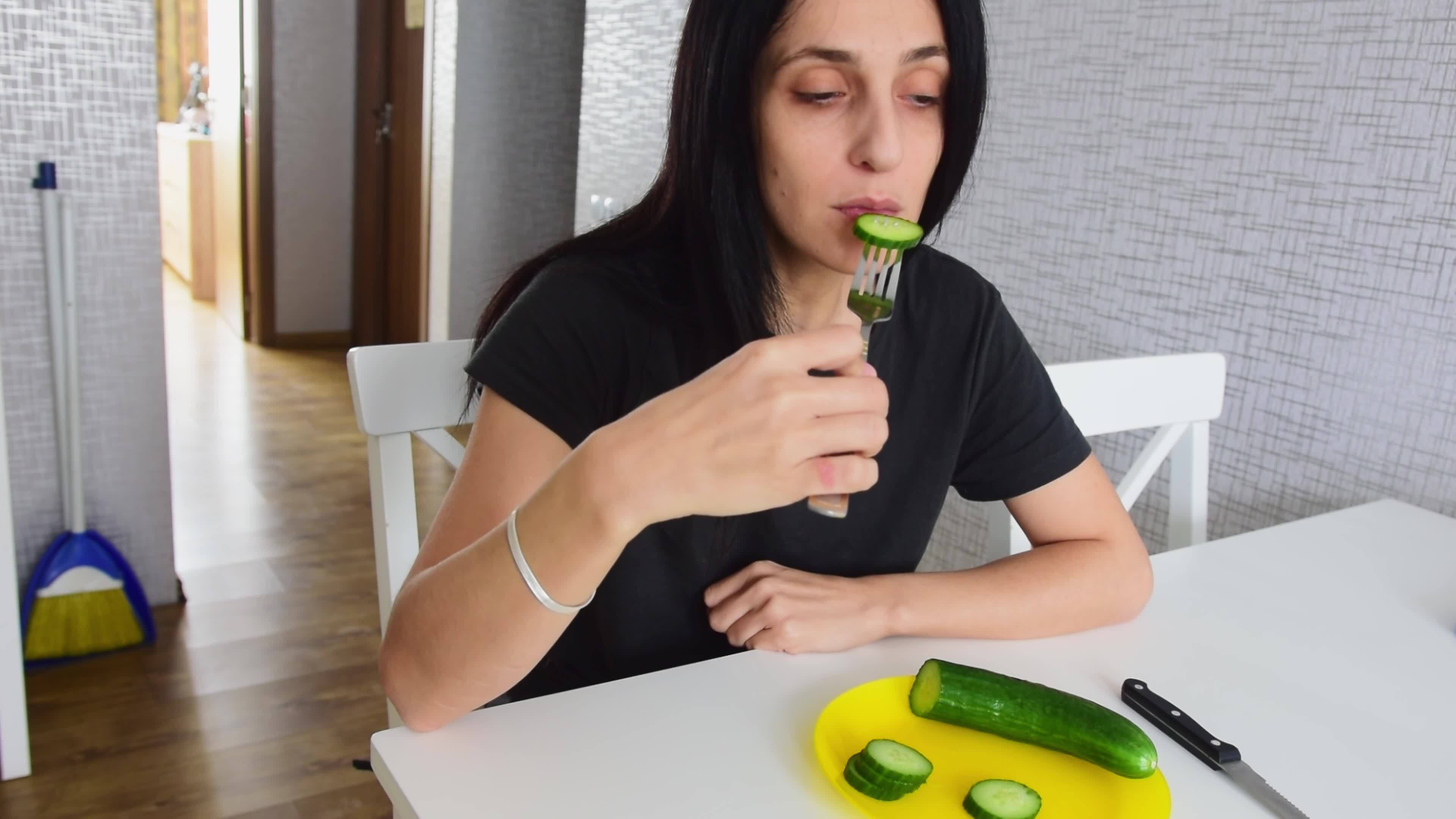 Portrait young attractive caucasian woman eat cucumber in kitchen