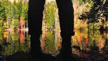 Close up low angle view silhouette of female legs and boots by scenic lake with outdoors in fall nature. Apparel in nature and autumn fashion concept