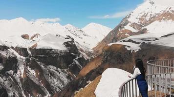 filmisk flygfoto zoom in i vy kvinna turist ser sig omkring med vördnad över utsikten över snösmältande täckta berg under våren video