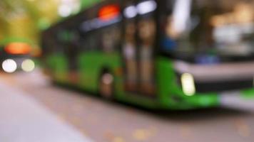 turva ônibus verde desfocado com luzes acesas na estrada movimentada do centro da cidade em dia nublado. fundo de transporte público com espaço em branco embaçado
