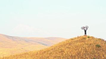 Isolated fit young caucasian male person lift bicycle up on hill with mountains background outdoors in caucasus mountains. Achievement , inspiration, challenge and determination concept video