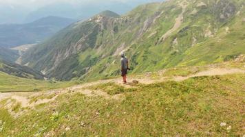 Aerial view of male person standing in scenic mountains and looking around with photo camera in hands.Location scouting for photography concept video