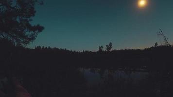 timelapse de la pleine lune se levant de jour en nuit à l'horizon avec une longue réflexion sur le lac geluva dans la nature de la campagne lituanienne video