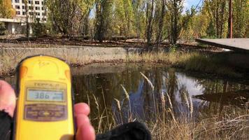 Chernobyl, Ukraine, 2019 - Close up of hand holding Geiger counter out of focus showing radiation levels by the pond in Chernobyl contaminated exclusion zone.