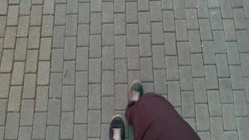 View down to male person legs and feet walking on grey pavement ground. Point of view perspective video