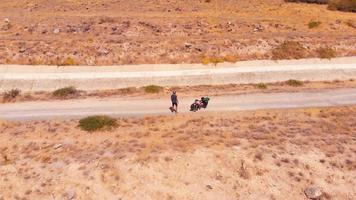 Aerial circle around solo cyclist on road with bicycle check map being lost outdoors in hot sunny day . Sportsman cyclist express emotions anger on road in public video