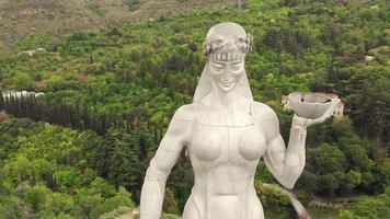 zoom aéreo fuera de la estatua de la madre de georgia en tbilisi con la naturaleza y el turista caminando en segundo plano video