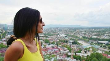 vista panorâmica jovem mulher caucasiana fica no ponto de vista aprecie o panorama cênico da cidade de tbilisi da fortaleza de narikala no verão. viajar na geórgia, cáucaso