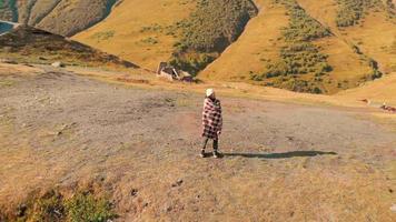 mujer caucásica está emocionada en las montañas con la iglesia de la trinidad kazbegi en el fondo. turismo y viajes en el cáucaso video
