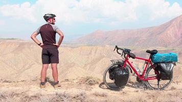 Statische Rückansicht Kaukasischer männlicher Radfahrer, der neben einem roten Tourenrad steht und auf den malerischen Berghintergrund blickt. aktives inspirierendes lifestyle-konzept