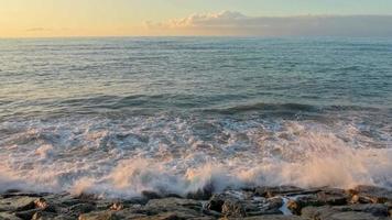 onde del mare al rallentatore si infrangono sulla costa rocciosa con sfondo azzurro del cielo sul tramonto spazio copia cinematografica vista sull'oceano video
