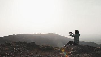 atractiva mujer morena con los brazos levantados sostiene un teléfono inteligente tomando una fotografía de vacaciones de las montañas del cáucaso. concepto de destino de viaje de georgia. video