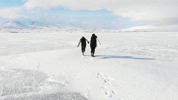 vista aérea trasera niño caucásico y madre joven divirtiéndose juntos compitiendo corriendo en la temporada de invierno vacaciones.lago congelado paravani, georgia video