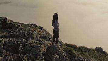 Aerial circle view of young confident female person standing on hill and enjoying scenic panorama above clouds video