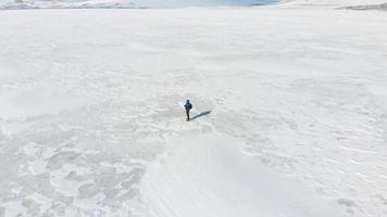 vue cinématographique aérienne une personne de sexe masculin se tient au milieu d'un champ de neige blanc pensif admirant la nature. concept de bien-être et de processus créatif video