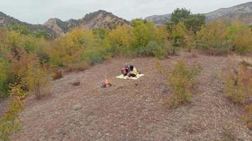 Young couple smile together by the fire spend time together outdoors isolated in wilderness video