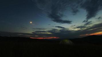 lasso di tempo della tenda verde da campeggio luminosamente illuminata che emette luce sul campeggio in montagne scure sotto il cielo coperto di stelle notturne. stile di vita attivo e concetto di viaggio. video