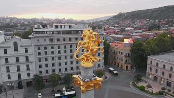 vuelo aéreo sobre la estatua dorada de san jorge de la plaza de la libertad con fondo de vista de la ciudad de tbilisi de la capital de georgia. video