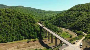 statische luchtfoto naar witte vrachtwagen op weg naar bosgroen in de bergregio van de Kaukasus. Logistiek en transportconcept video