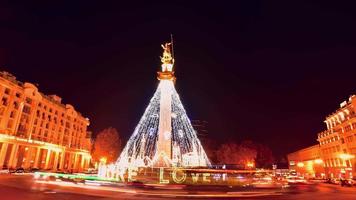 auto statiche timelapse passano sulla rotonda lasciando scie luminose con albero di Natale decorato sulla piazza della libertà e turisti che scattano fotografie