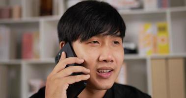 Closeup face of smiling asian man talking on mobile phone at home. Cheerful businessman having phone call at workplace. Portrait of happy business man calling phone indoor.