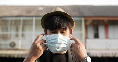 close-up van een jonge aziatische man met kort haar die een beschermend medisch gezichtsmasker draagt en op straat staat. man met beschermende maskers, tijdens covid-19-noodsituatie. reis- en levensstijlconcept.