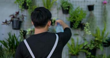 portrait d'un jeune jardinier asiatique debout et arrosant les plantes. l'homme a tourné le dos pour regarder la caméra et sourire. concept de verdure, de passe-temps et de style de vie à la maison. video