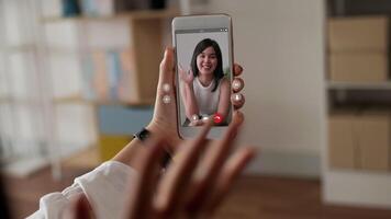 cierra la mano de una mujer feliz sosteniendo un teléfono móvil y chateando por skype con un amigo. joven asiática que tiene una videollamada a través de un teléfono inteligente hablando con un amigo. Internet y tecnología en línea. video