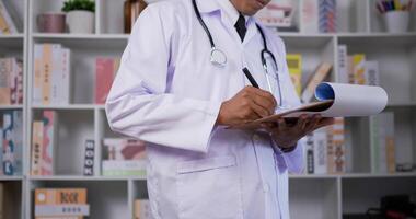 Close up side view of Confident male doctor writing the medical report on clipboard while standing in clinic. Man filling up medical form on a note. Healthcare, insurance and medicine concept. video