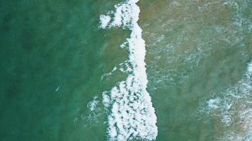 Aerial view of white sand beach and water surface texture. Foamy waves with sky. Beautiful tropical beach. Amazing Sandy coastline with white sea waves. Nature, seascape and summer concept. Zoom out.