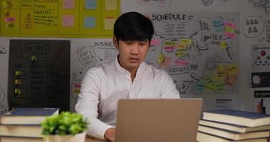 Porträt eines professionellen asiatischen Geschäftsmannes, der hustet, während er zu Hause am Laptop arbeitet. Mann sitzt am Schreibtisch am Arbeitsplatz. kranker mann, der computernotizbuch tippt. Gesundheitskonzept. video
