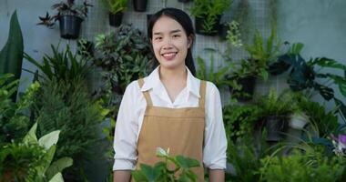 el retrato de la dueña de una jardinera asiática con mascarilla está cruzando el brazo y mirando la cámara en el jardín. vegetación doméstica, venta en línea y concepto de hobby. video