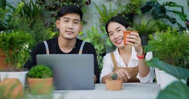 retrato de um feliz jardineiro jovem casal asiático vendendo on-line nas mídias sociais e olhando para a câmera no jardim. selfie de homem e mulher com telefone celular. verdura em casa, venda online e hobby. video