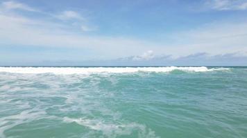 praia de areia do oceano azul e textura da superfície da água. ondas espumosas com céu e nuvens. bela praia tropical. incrível litoral arenoso com ondas do mar branco. conceito de natureza, marinha e verão.