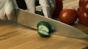 las manos de las mujeres están usando un cuchillo de cocina para cortar un pepino verde fresco en una tabla de cortar de madera. alimentación saludable. pepino verde en rodajas, video