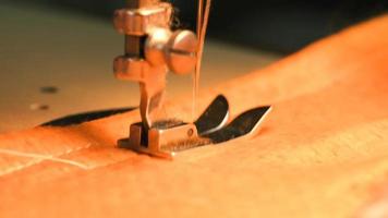 The needle of the sewing machine makes a stitch with a thread. Sewing orange fabric on a sewing machine in slow motion in macro photography video