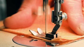 The needle of the sewing machine makes a stitch with a thread. Sewing orange fabric on a sewing machine in slow motion in macro photography video