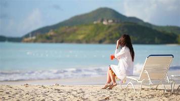 jeune femme avec verre à cocktail sur la plage blanche assise sur un lit de bronzage video