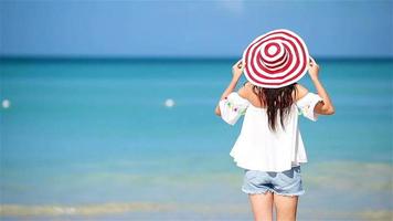 junge schöne Frau am tropischen Strand mit weißem Sand. Rückansicht des kaukasischen Mädchens im Hut Hintergrund das Meer