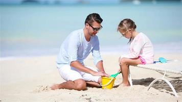 padre y niña haciendo castillos de arena en la playa tropical video